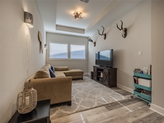 living room with a raised ceiling, visible vents, baseboards, and wood finished floors