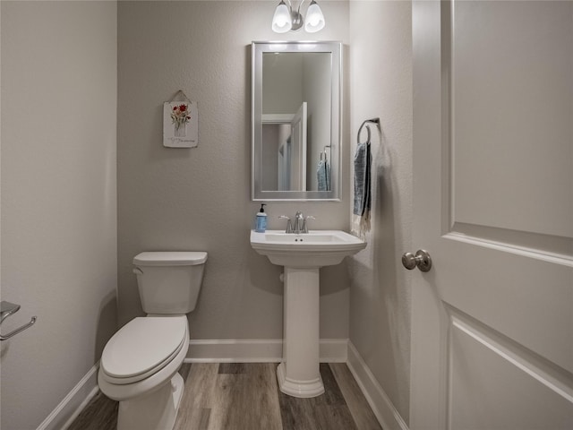 half bathroom featuring baseboards, a sink, toilet, and wood finished floors