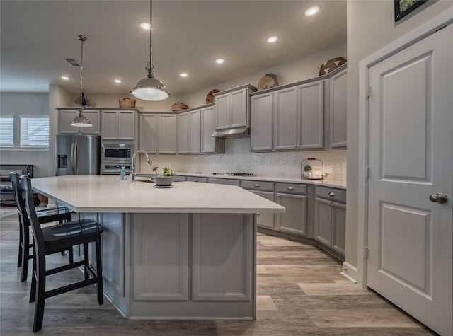 kitchen with stainless steel appliances, a kitchen breakfast bar, backsplash, gray cabinets, and a center island with sink