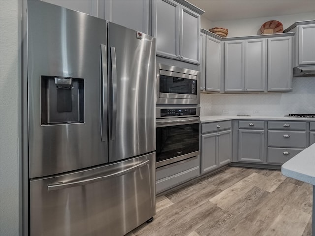 kitchen featuring light wood finished floors, gray cabinets, stainless steel appliances, light countertops, and backsplash