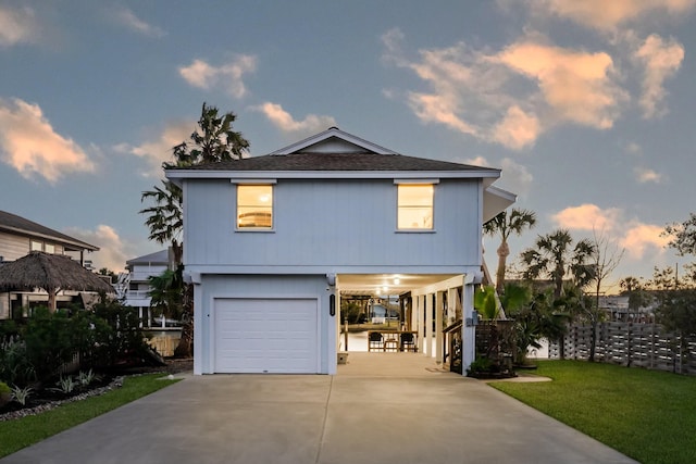 coastal inspired home featuring roof with shingles, a garage, a carport, driveway, and a front lawn