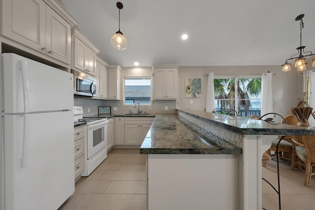 kitchen featuring white appliances, a sink, white cabinets, a kitchen bar, and decorative light fixtures