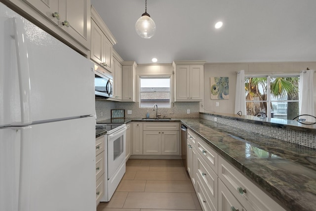 kitchen with dark stone counters, appliances with stainless steel finishes, decorative light fixtures, white cabinetry, and a sink