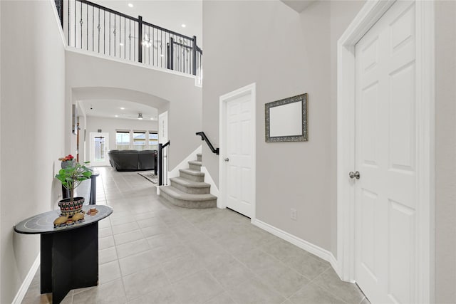 foyer featuring arched walkways, a high ceiling, baseboards, and stairs