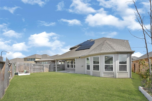 back of house with a yard, roof with shingles, and roof mounted solar panels