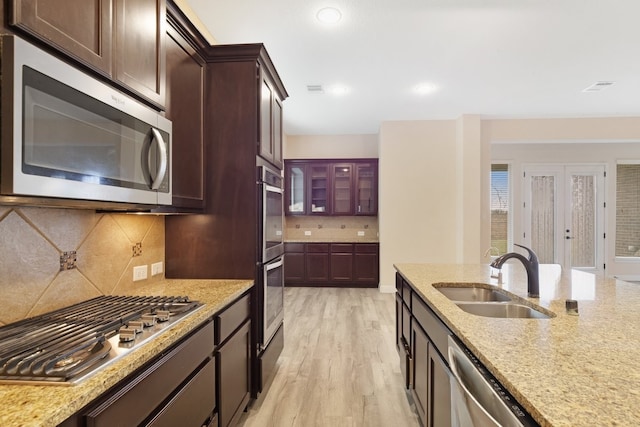 kitchen featuring backsplash, appliances with stainless steel finishes, light wood-style floors, a sink, and light stone countertops