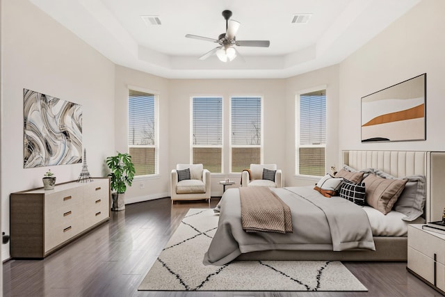 bedroom featuring baseboards, visible vents, a tray ceiling, and wood finished floors