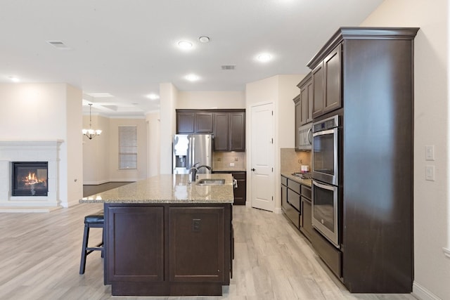 kitchen with a breakfast bar area, visible vents, decorative backsplash, appliances with stainless steel finishes, and dark brown cabinets