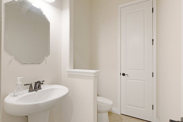 half bathroom with a sink, tile patterned flooring, and toilet