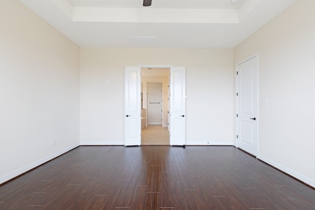 spare room with a tray ceiling, baseboards, and dark wood-style flooring