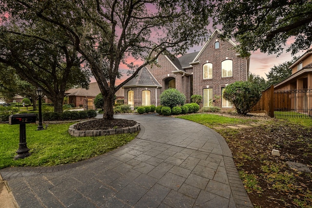 view of front of home featuring brick siding, curved driveway, a front yard, and fence