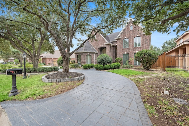 view of front facade featuring brick siding, curved driveway, a front yard, and fence