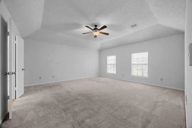 carpeted empty room featuring a textured ceiling, a ceiling fan, visible vents, baseboards, and a raised ceiling