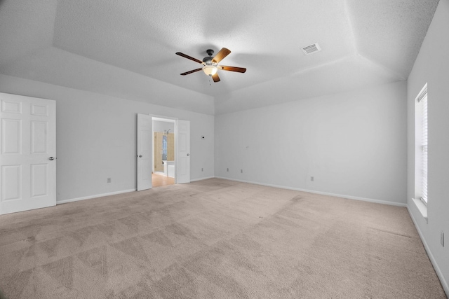 empty room with a tray ceiling, visible vents, light carpet, a textured ceiling, and baseboards