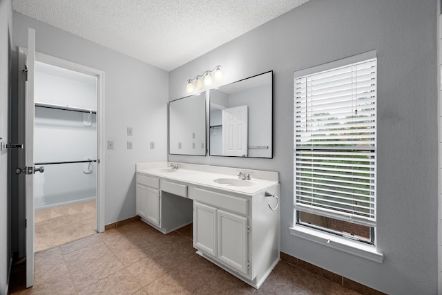 bathroom with a textured ceiling, double vanity, a spacious closet, and a sink