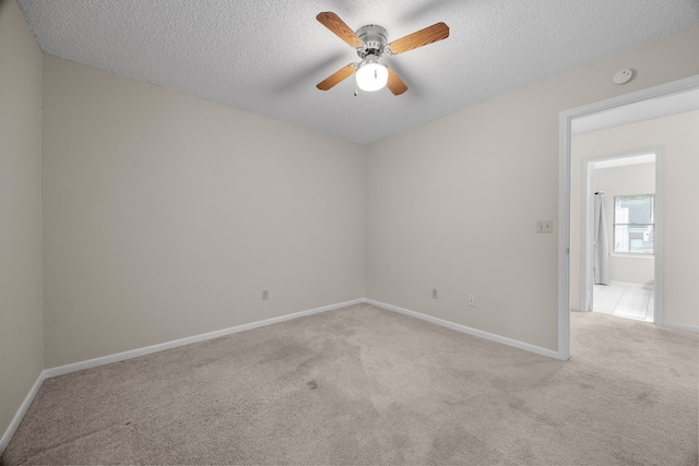 spare room with light carpet, a textured ceiling, a ceiling fan, and baseboards