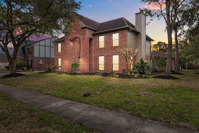 view of front facade featuring a chimney, a lawn, and brick siding