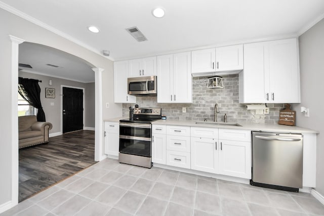 kitchen with arched walkways, a sink, light countertops, appliances with stainless steel finishes, and decorative columns