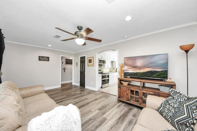 living area featuring light wood finished floors, visible vents, arched walkways, and crown molding