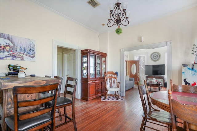 dining space with ornamental molding, wood-type flooring, visible vents, and a notable chandelier