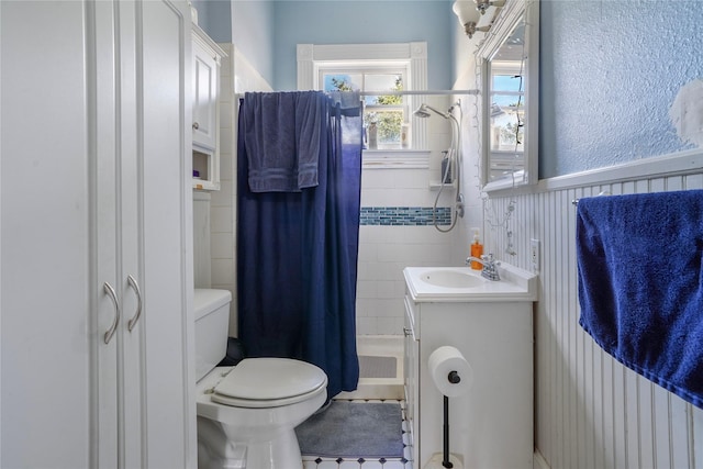 full bathroom with toilet, a wainscoted wall, shower / bath combo with shower curtain, vanity, and tile walls