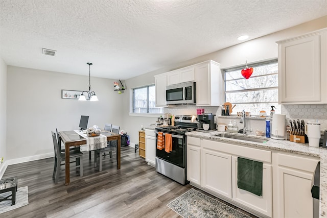 kitchen featuring visible vents, light wood-style flooring, a sink, stainless steel appliances, and backsplash