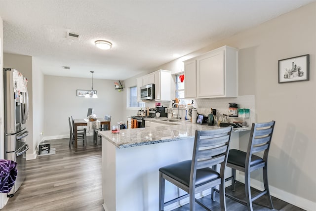 kitchen featuring a peninsula, a sink, visible vents, appliances with stainless steel finishes, and light stone countertops