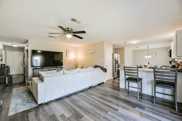 living room featuring a ceiling fan, dark wood-style flooring, visible vents, and a textured ceiling