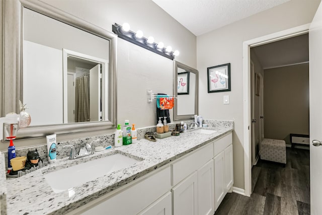 full bathroom with double vanity, wood finished floors, a sink, and baseboards