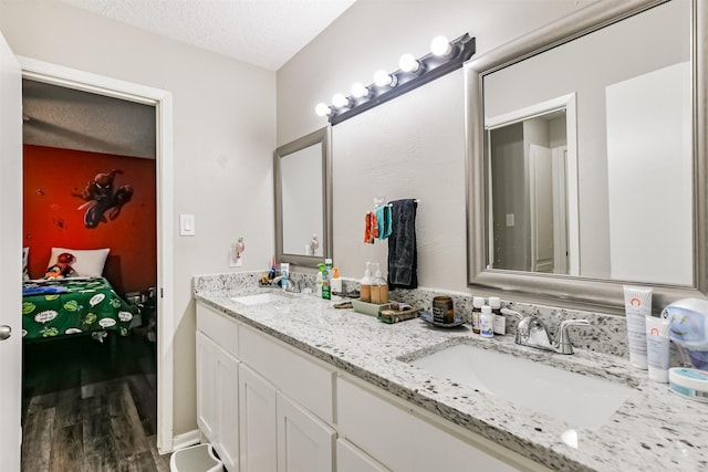 bathroom with a textured ceiling, double vanity, wood finished floors, and a sink