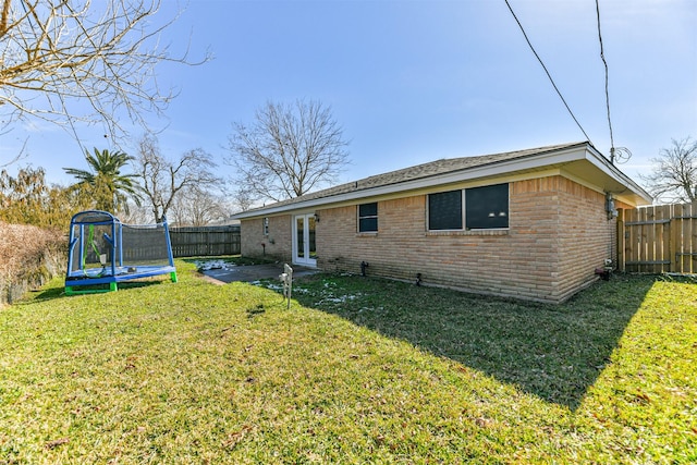 rear view of property featuring a fenced backyard, brick siding, french doors, a lawn, and a trampoline