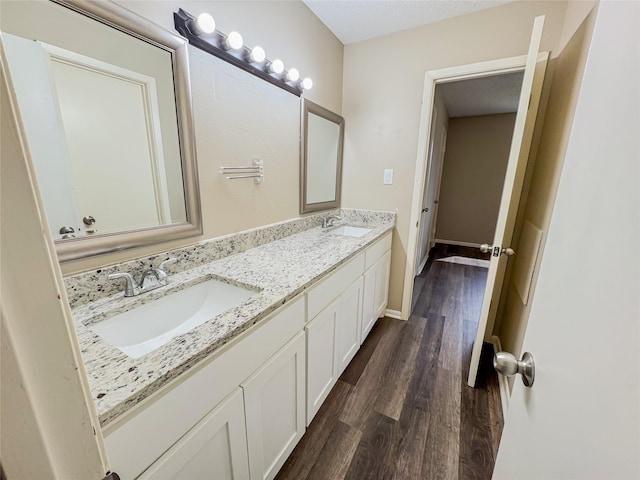 full bath with double vanity, wood finished floors, a sink, and baseboards