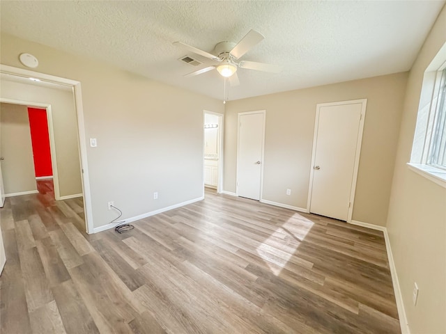 unfurnished bedroom featuring light wood-type flooring, visible vents, a textured ceiling, and baseboards