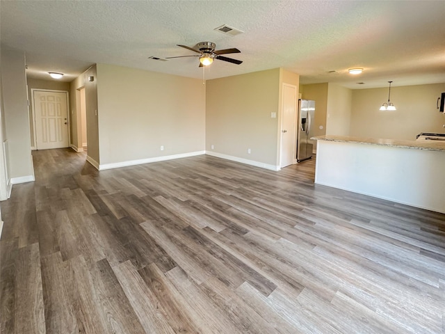 unfurnished living room featuring dark wood-style floors, visible vents, a textured ceiling, baseboards, and ceiling fan with notable chandelier