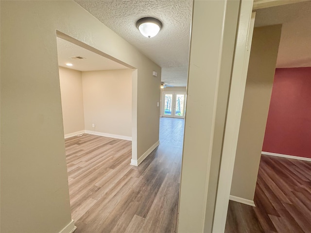 hall with visible vents, baseboards, wood finished floors, a textured ceiling, and french doors