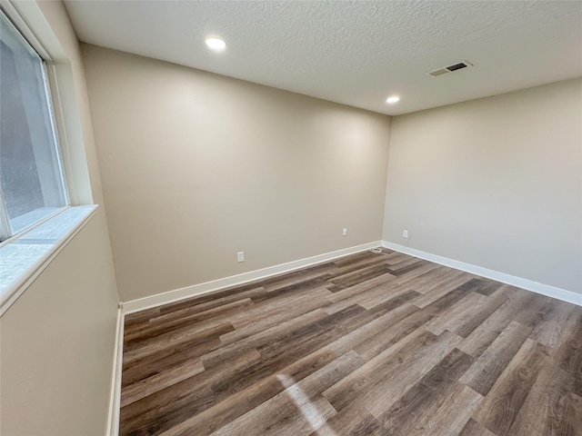 empty room with visible vents, baseboards, dark wood finished floors, and a textured ceiling