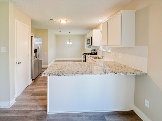 kitchen with light stone counters, stainless steel appliances, a peninsula, a sink, and light wood-type flooring