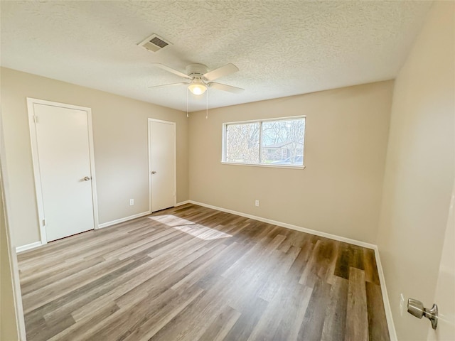 unfurnished bedroom featuring baseboards, visible vents, ceiling fan, wood finished floors, and a textured ceiling