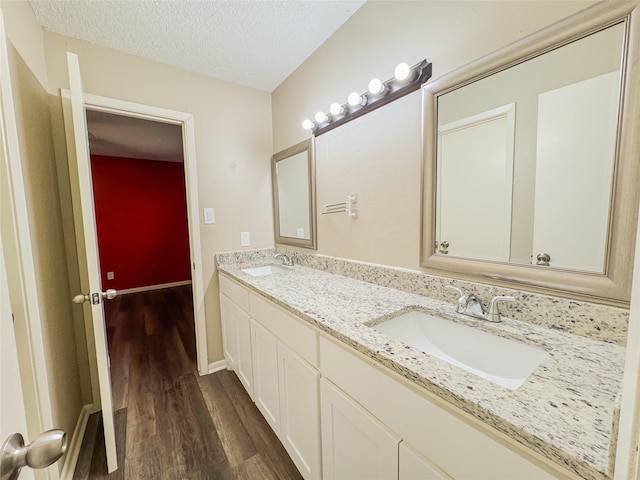 bathroom featuring double vanity, a textured ceiling, a sink, and wood finished floors