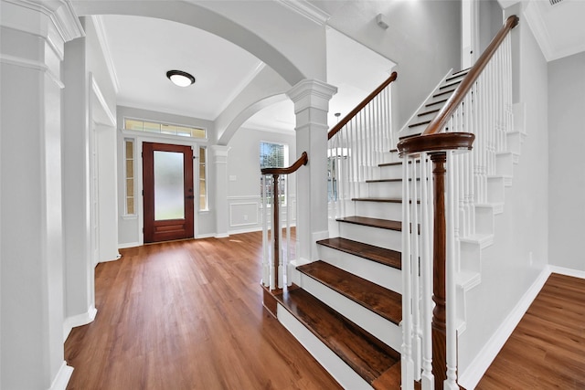 foyer entrance with arched walkways, baseboards, ornamental molding, wood finished floors, and ornate columns