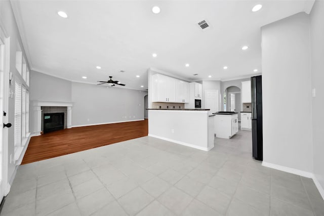 kitchen with visible vents, arched walkways, a glass covered fireplace, dark countertops, and crown molding