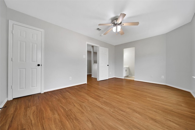 unfurnished bedroom with a walk in closet, visible vents, ceiling fan, wood finished floors, and baseboards