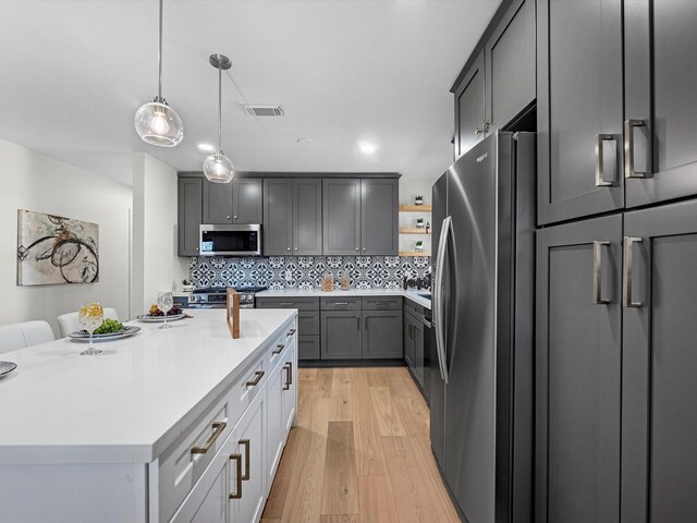 kitchen featuring decorative light fixtures, light countertops, backsplash, appliances with stainless steel finishes, and light wood-type flooring
