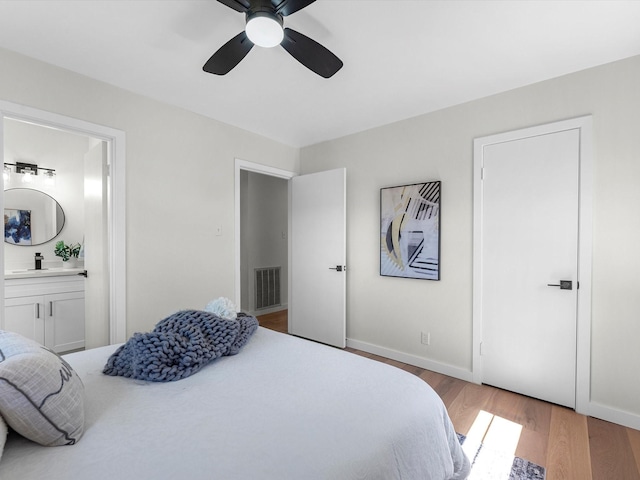 bedroom featuring light wood finished floors, visible vents, ensuite bathroom, a ceiling fan, and baseboards