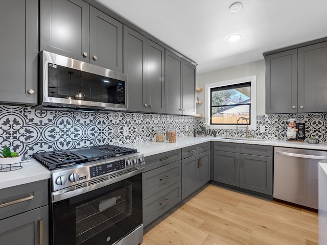 kitchen featuring a sink, light countertops, appliances with stainless steel finishes, light wood-type flooring, and gray cabinets