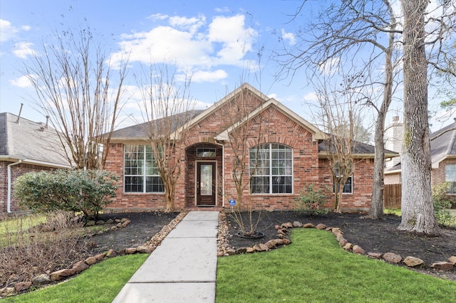 ranch-style home featuring brick siding, a front lawn, a shingled roof, and fence