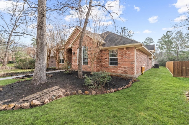 view of side of property featuring a yard, brick siding, roof with shingles, and fence