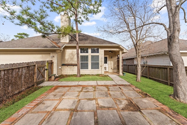 back of house featuring a shingled roof, a patio, a fenced backyard, a chimney, and a yard