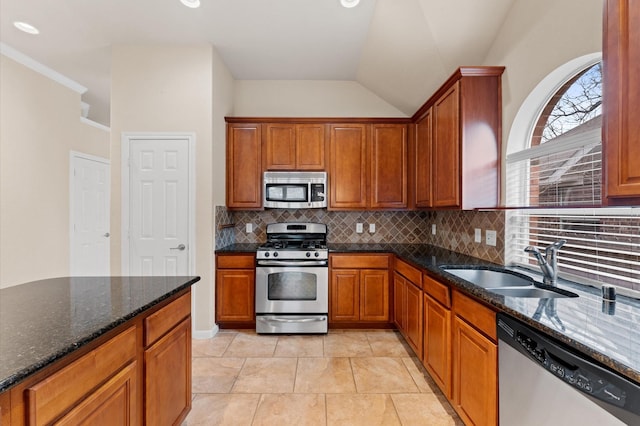 kitchen with tasteful backsplash, brown cabinetry, dark stone countertops, stainless steel appliances, and a sink