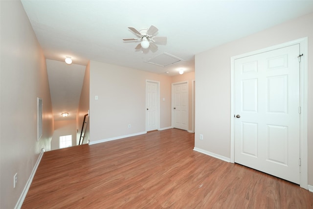 empty room featuring visible vents, light wood-type flooring, attic access, and baseboards